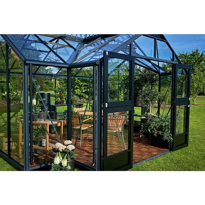 Juliana Gewächshaus Orangerie - Außenmaß inkl. Dachüberstand (B x T): 439 x 373 cm, Material Seitenwand: Glas, 3 mm, Anthrazit/Schwarz - Ein Gewächshaus mit geöffneten Türen, eingerichtet mit einem Tisch und Stühlen, umgeben von Pflanzen und Blumen, die eine einladende Atmosphäre schaffen.