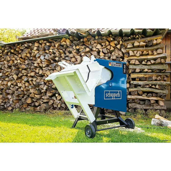 Scheppach Wippkreissäge HS720 - 4.500 W, Durchmesser Sägeblatt: 700 mm - Scheppach Wippsäge auf Rasen vor Holzstapel. Die Säge ist blau und weiss und hat Räder für den Transport.