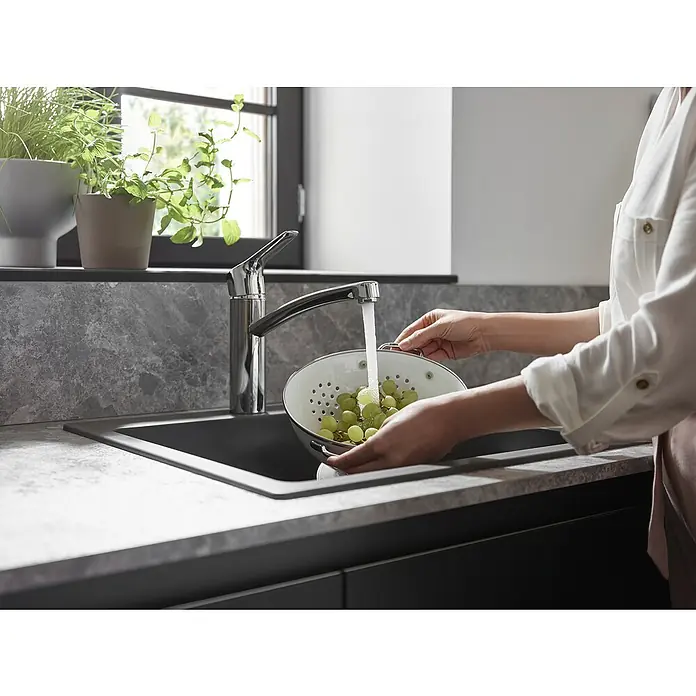 Hansgrohe MySport Grifo de cocina M - Cromo, Brillante - Una persona lava uvas verdes en un colador blanco bajo un grifo moderno en una cocina elegante.