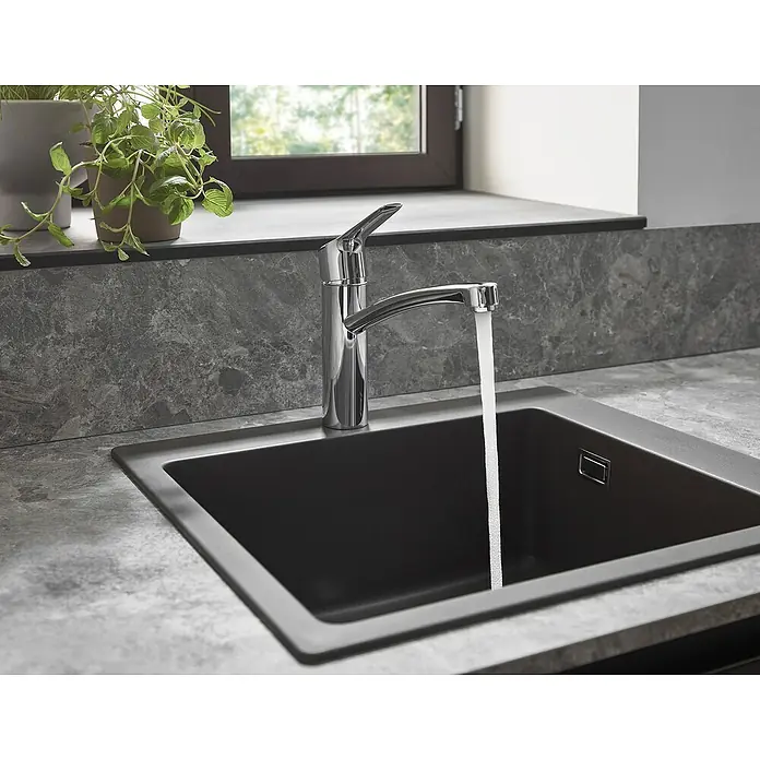 Hansgrohe MySport Grifo de cocina M - Cromo, Brillante - Primer plano de un fregadero de cocina moderno con agua corriente y una planta al fondo. El diseño es elegante y sobrio.