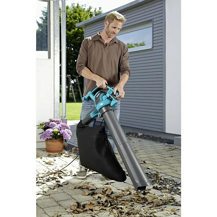 Gardena Aspirador de hojas eléctrico Ergojet 3000 - 3.000 W, Velocidad de soplado: 310 km/h - Un hombre está usando un aspirador/soplador de hojas Gardena en el jardín para quitar las hojas. El dispositivo es verde azulado con una bolsa negra.