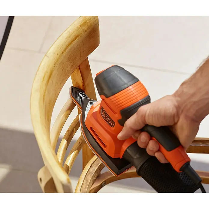 Black+Decker Lijadora multifunción eléctrica  BEW200-QS - 200 W, Número de oscilaciones marcha en vacío: 12.000 r.p.m., Diámetro circuito oscilante: 2 mm - Primer plano de una lijadora de detalle Black+Decker lijando una silla de madera, diseñada para trabajos de precisión.