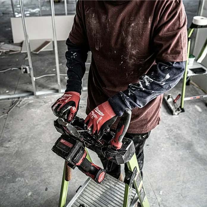 Little Giant Stehleiter MIGHTYLITE 3 Stufen - Anzahl Tritte: 3 Stk., Arbeitshöhe: 284 cm, Belastbarkeit: 150 kg, Verbundwerkstoff - Der Handwerker benutzt ein Milwaukee-Elektrowerkzeug, um an einem Bauprojekt zu arbeiten. Er steht auf einer grünen Leiter und trägt schützende Handschuhe.