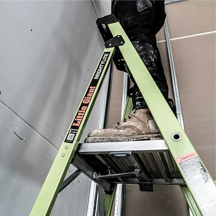Little Giant Stehleiter MIGHTYLITE 2 Stufen - Anzahl Tritte: 2 Stk., Arbeitshöhe: 280 cm, Belastbarkeit: 150 kg, Verbundwerkstoff - Nahaufnahme einer Little Giant-Leiter, die ein Arbeiter in Arbeitskleidung benutzt. Die Leiter scheint robust und für den Baueinsatz geeignet.