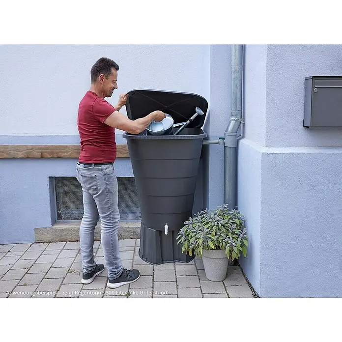 Garantia Regentonnensockel - Passend für: Garantia Regentonne 210 Liter rund, Regentonne 203 + 300 Liter eckig in Anthrazit - Der Mann befüllt eine 300-Liter-Regentonne mit Gießkanne. Praktische Wasserspeicherung für den Garten.