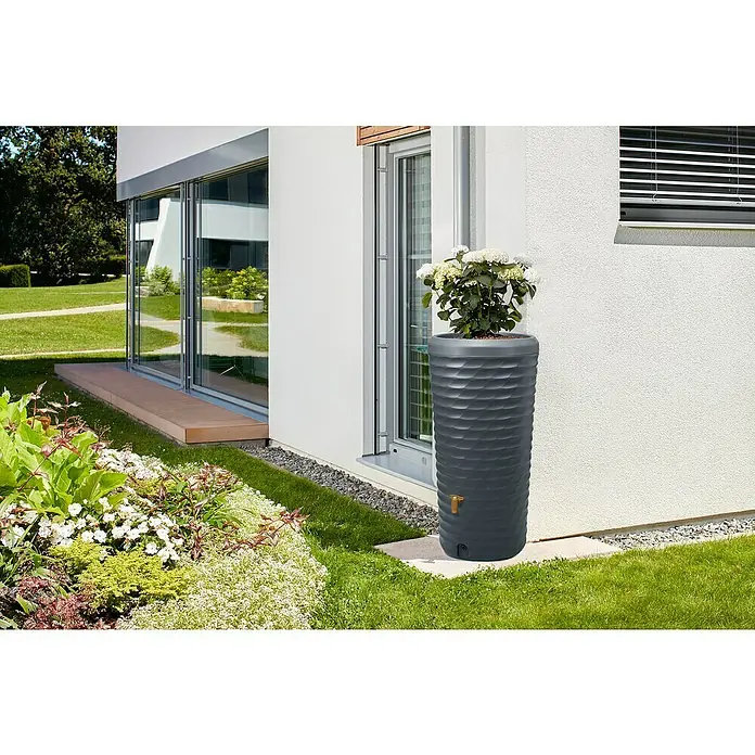 4rain Regenspeicher Jolie - 230 l, Graphitgrau, 1 Stk. - Eine graue Regentonnen-Säule mit Pflanzschale steht vor einer weißen Hauswand und dient als dekorativer Wasserspeicher für den Garten.