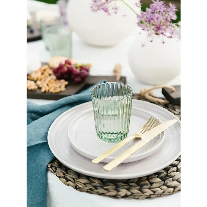 Trinkglas Blossom - 4 Stk., Fassungsvermögen: 0,26 l, Grün - Nahaufnahme von einem gedeckten Tisch mit einem gerippten Glas, goldenem Besteck und einem weißen Teller auf einem geflochtenen Tischset.