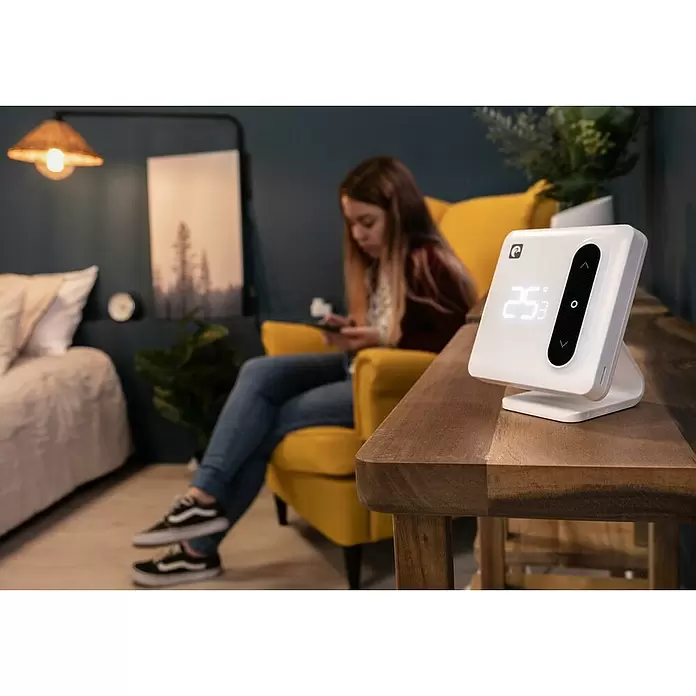Garza Termostato inalámbrico Smart Aspen - Blanco - Termostato inteligente blanco mostrando 25,3°C con controles de subir/bajar, sobre una mesa de madera en un salón.