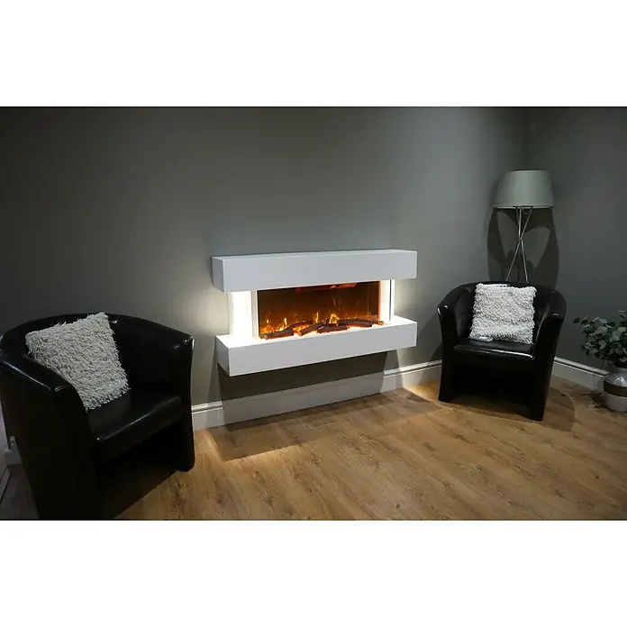 Focalpoint Chimenea eléctrica Ashford Wall Suite - Blanco, 2.000 W, 26,5 x 122 x 60 cm - Un salón moderno con una chimenea eléctrica blanca montada en la pared, flanqueada por dos sillones negros con cojines.