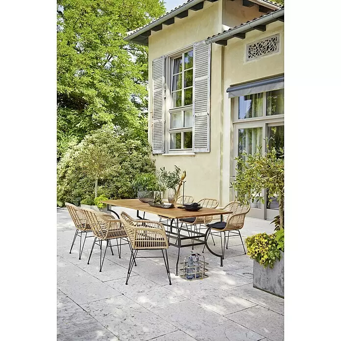 Sunfun Moni Gartentisch - L x B x H: 220 x 100 x 77 cm, Akazie, Stahl, Rechteckig, Natur, Schwarz - Outdoor-Essgruppe mit Holztisch und Korbstühlen mit schwarzen Kissen, auf einer Terrasse neben einem Haus mit Grünflächen.