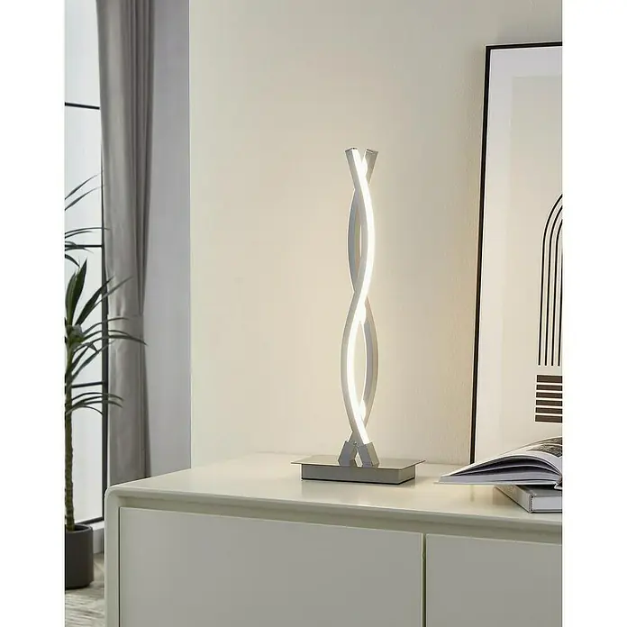 Eglo Lámpara de sobremesa LED Lasana 2 - 10 W, L x An x Al: 16 x 10 x 46 cm, Cromo, Blanco cálido - Primer plano de una moderna lámpara de mesa LED en espiral plateada, que emite una luz cálida y brillante, colocada sobre una mesita de noche blanca.