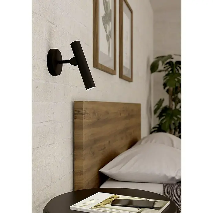 Aplique LED Almudaina - 5 W, L x Al: 11 x 20 cm, Negro, Blanco cálido - Lámpara de pared LED negra mate giratoria para el dormitorio, montada en una pared de ladrillo blanco sobre una mesita de noche.