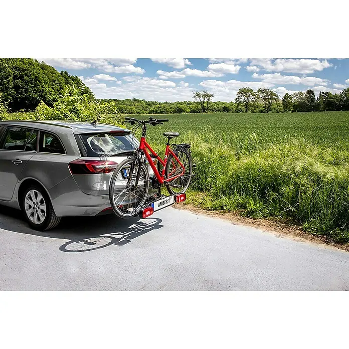 Eufab Fahrradträger Amber I - Geeignet für: 1 Fahrrad, Passend für: Fahrzeuge mit Anhängerkupplung - Ein graues Auto mit einem Fahrradträger, auf dem ein rotes Fahrrad befestigt ist, auf einer Straße.