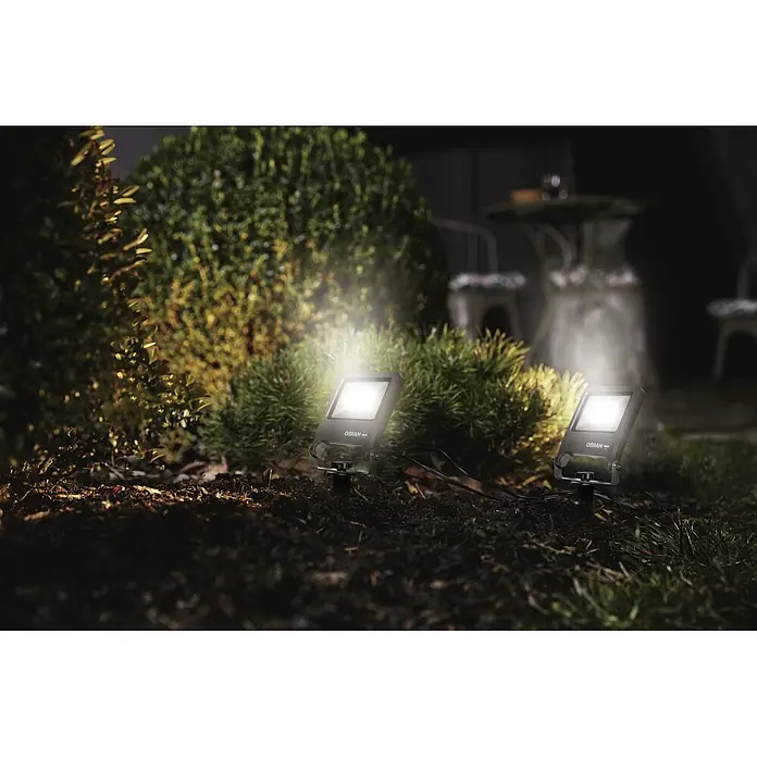 Ledvance LED-Gartenstrahler Endura Floodspike - 10 W, 800 lm, 3.000 K, 4,4 x 10,8 x 29,2 cm, IP65 - Zwei LED-Gartenstrahler von OSRAM beleuchten Büsche in einem Garten bei Nacht.