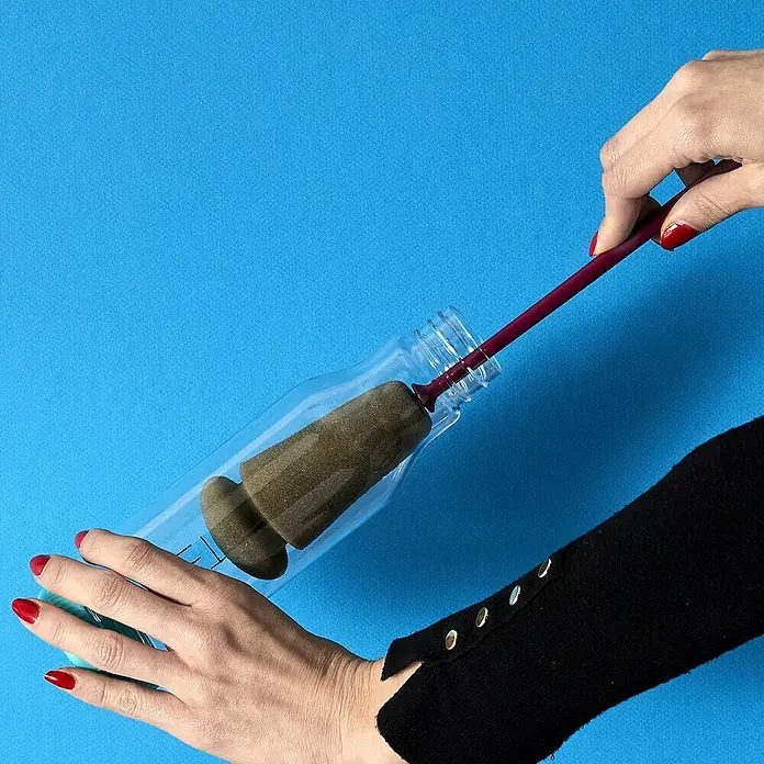 Esponja limpiadora de botellas - Ø x Al: 5,5 x 34,5 cm - Una botella se está limpiando con un cepillo para biberones, que cuenta con un mango largo y un cabezal de esponja para una limpieza eficaz.