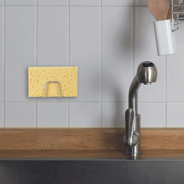 Soporte de esponja - Acero inoxidable, 1 ud. - Soporte de esponja con esponja amarilla en una pared de azulejos junto a un grifo, práctica organización de la cocina.