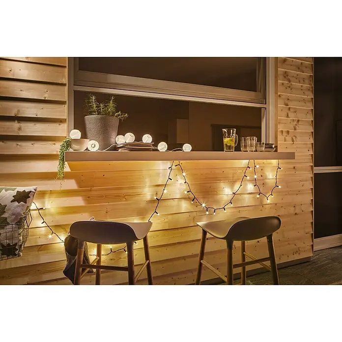 Paulmann Guirnalda luminosa LED Lampion - 3,6 m, Para exterior - Un patio con paneles de madera decorado con luces y elegantes taburetes de bar, creando un ambiente acogedor.