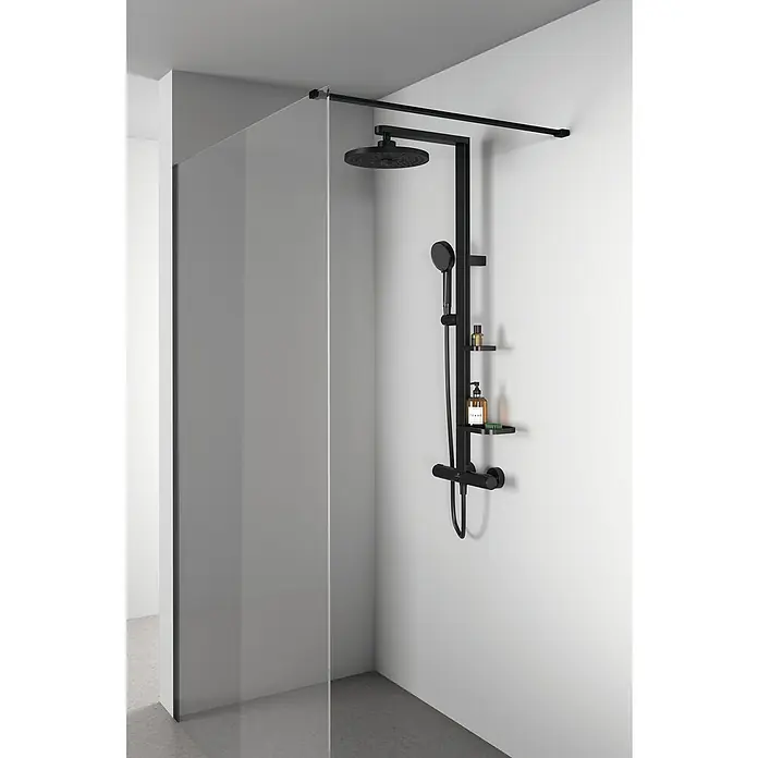 Ideal Standard Überkopfbrausen-Set Alu+ - Schwarz, Durchmesser Kopfbrause: 26 cm - Schwarze Duschsäule mit Kopf- und Handbrause sowie zwei Ablagen. Das Duschsystem ist an einer weißen Wand neben einer Duschkabine montiert.