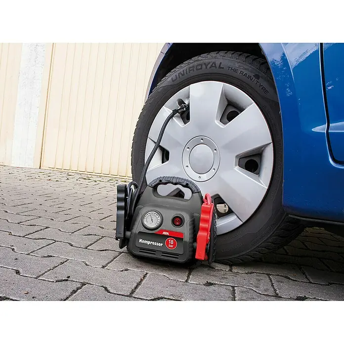 APA Energiestation Powerpack Max 500A Starthilfe - Kapazität: 7 Ah - Eine APA-Luftpumpe "Kompressor 18 bar" wird zum Aufpumpen eines blauen Autoreifens verwendet, der vor einer Garagenwand steht.