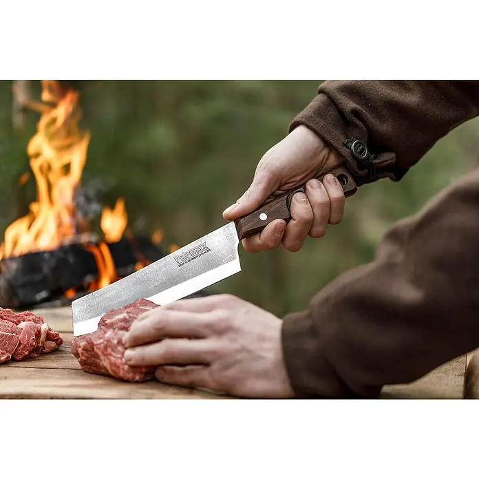 Petromax Küchenmesser - Stahl, 31,5 cm - Nahaufnahme einer Person, die mit einem scharfen, rechteckigen Kochmesser von TEPPOMAX Fleisch auf einem Holzbrett schneidet.