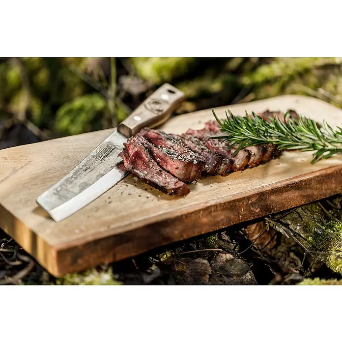Petromax Küchenmesser - Stahl, 31,5 cm - Ein appetitliches, tranchiertes Steak auf einem Holzbrett mit einem Messer, garniert mit Rosmarin, für den Feinschmecker.