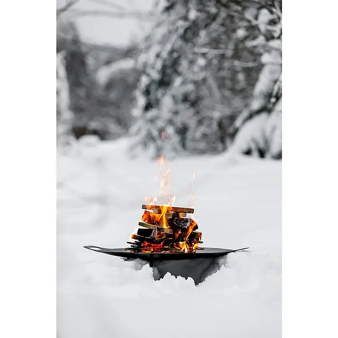 Petromax Feuerschale - Durchmesser: 48 cm, Stahl - Ein Lagerfeuer brennt auf einem schwarzen Grill inmitten einer schneebedeckten Landschaft. Die Flammen tanzen um das Holz.
