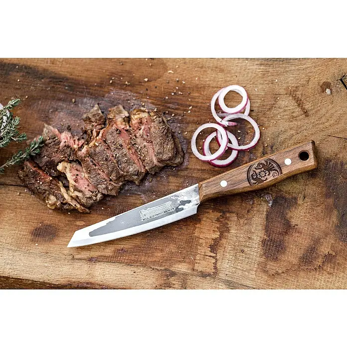 Petromax Allzweckmesser - Stahl, Länge: 28 cm - Das Feiromaxx Messer auf einem Holzbrett mit aufgeschnittenem Steak und Zwiebelringen.