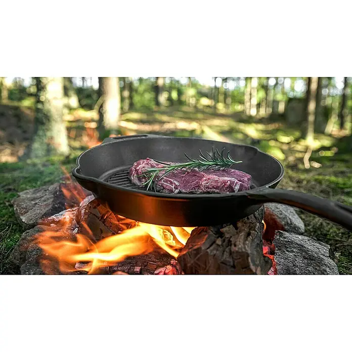 Petromax Grillpfanne - Durchmesser: 30 cm, Höhe: 4,8 cm, Gusseisen - Gegrilltes Steak mit Rosmarin in einer gusseisernen Pfanne über offenem Feuer, umgeben von Bäumen.