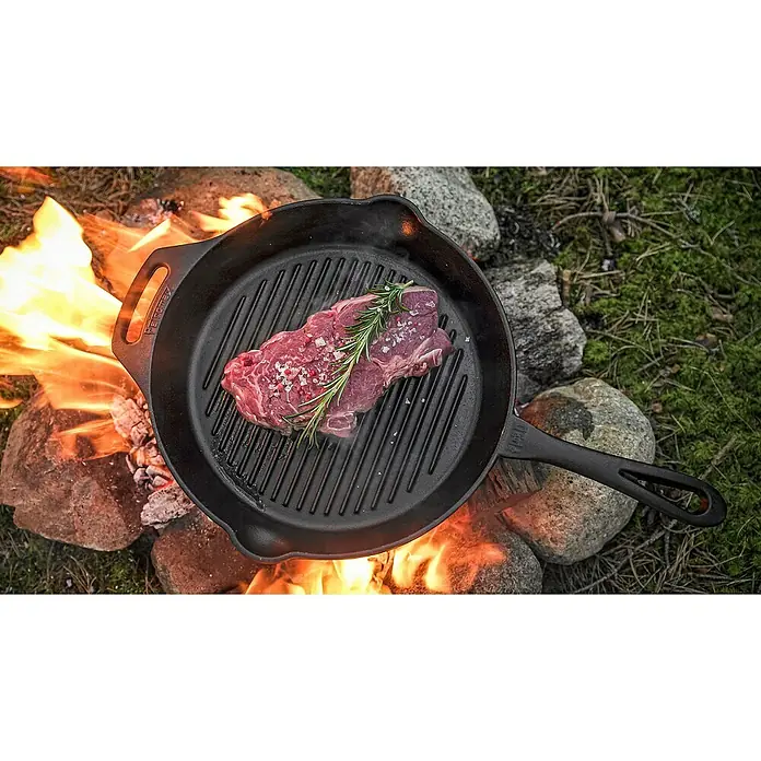 Petromax Grillpfanne - Durchmesser: 30 cm, Höhe: 4,8 cm, Gusseisen - Ein saftiges Steak mit Rosmarin und grobem Salz auf einer schwarzen Grillpfanne über offenem Feuer, bereit zum Brutzeln.