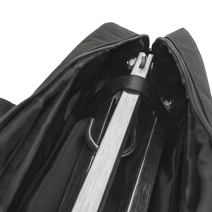 Petromax Transporttasche Dreibeinständer - Nylon, Passend für: Petromax Dreibeinständer - Nahaufnahme einer schwarzen Tragetasche mit einem darin verstauten, zusammengeklappten Holzständer, gesichert mit einem Gurt.