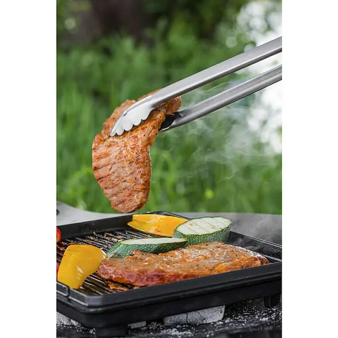 Petromax Grillzange - Länge: 41 cm, Edelstahl - Ein saftiges Steak wird mit einer Grillzange über einem heißen Grill mit Gemüse gewendet.