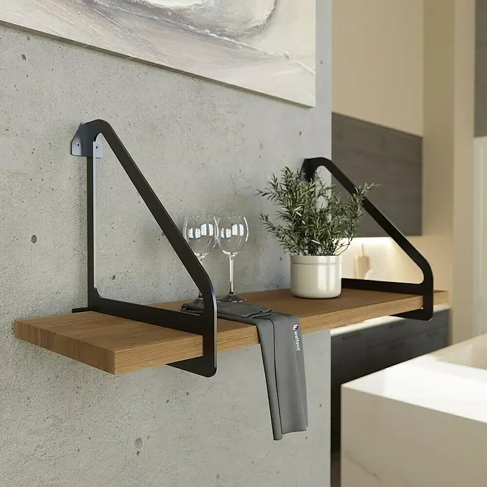 Walteco Wandkonsole Inspira - L x B x H: 26 x 23,4 x 26 cm, Stahl, Mattschwarz - Nahaufnahme eines modernen Holzregals mit schwarzen Metallhalterungen an einer grauen Wand, dekoriert mit Gläsern und einer Pflanze.