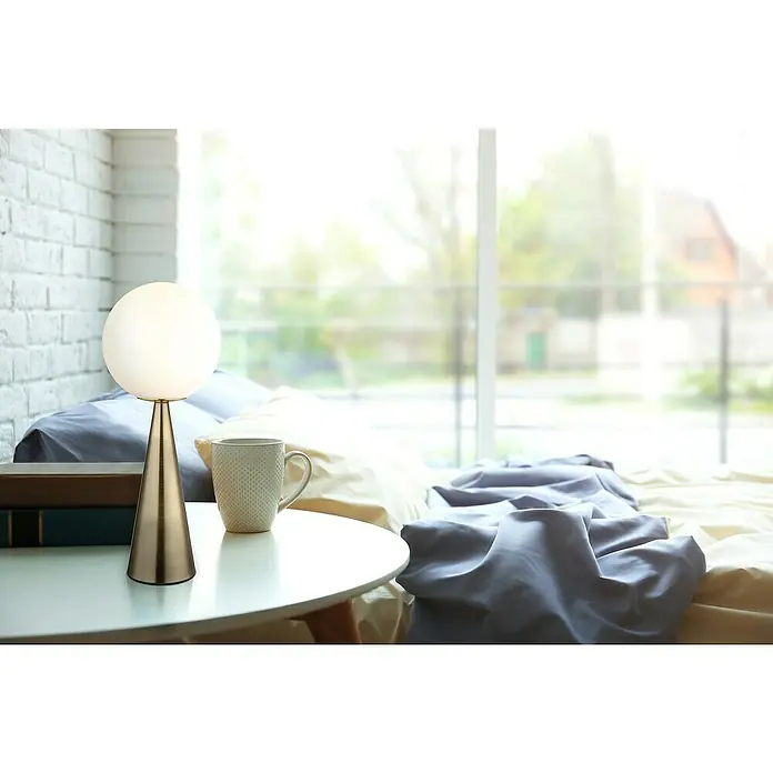 Globo Tischleuchte Pinapl - 40 W, Ø x H: 20 x 49,5 cm, Messingfarben matt, Weiß opal - Nahaufnahme einer modernen Tischlampe mit kugelförmigem Lampenschirm und goldenem Sockel auf einem Nachttisch im Schlafzimmer.