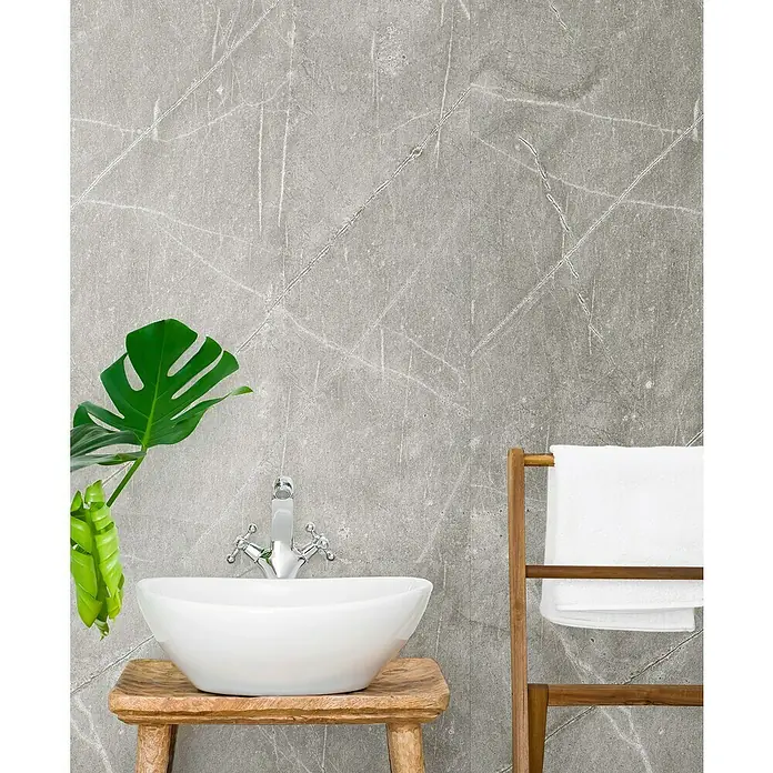LOGOCLIC Wandpaneel Designwall - Grey Atlantic Marble, 265 x 123 cm - Elegantes Badezimmer-Interieur mit einem runden Waschbecken auf einem Holzschemel, einem Handtuchhalter und einer grünen Pflanze vor einer grauen Steinwand.