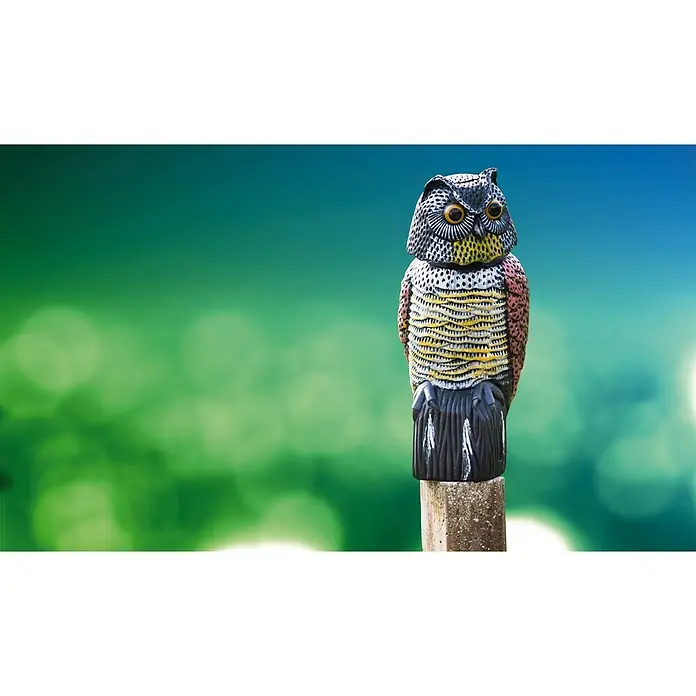 Altadex Búho Espanta pájaros - Altura: 41 cm - Un señuelo de búho detallado posado en un poste, ideal para el control de aves y la decoración del jardín, sobre un fondo verde borroso.