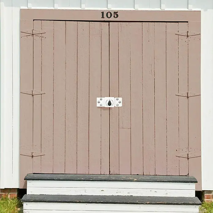 Abus Diskus Candado de disco 141/200+20/70 - An x Al: 22 x 8,5 cm, Acero - Primer plano de una puerta de madera con el número 105, con herrajes decorativos y un cerrojo blanco que realza su encanto rústico.