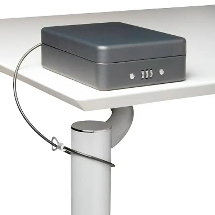 Arregui Caja de caudales Private C-9427 - L x An x Al: 20,3 x 15 x 6,5 cm, Negro - Imagen de una caja fuerte portátil gris con cerradura de combinación y cable de seguridad conectado a una pata de mesa blanca.