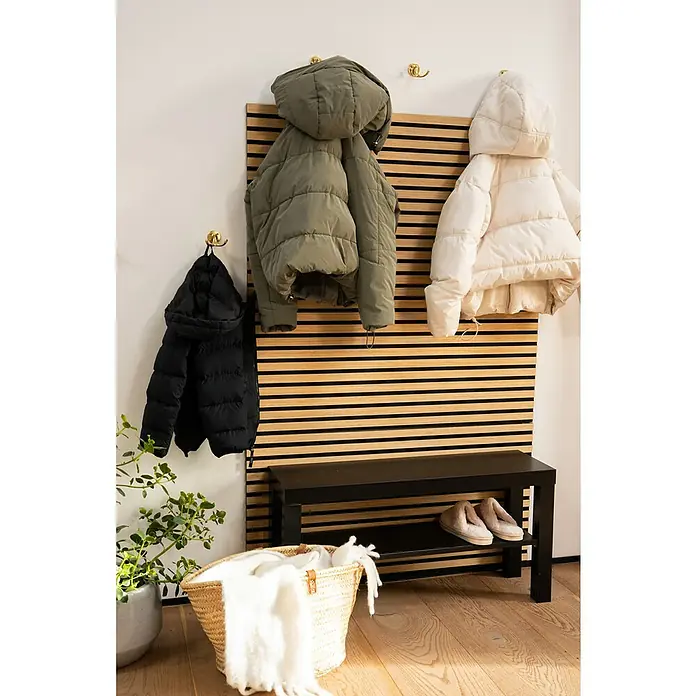 Jangal Akustikpaneel Modular Wall Furnier - Fanal Oak, 1.040 x 520 x 10 mm - Eine stilvolle Garderobe mit einer schwarzen Bank, einer Holzwand und farblich passenden Jacken in Schwarz, Olivgrün und Beige.