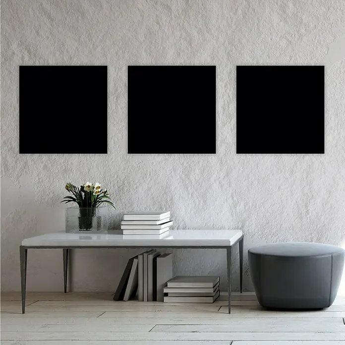 Jangal Wandpaneel Modular Wall PET Filz - Black, 520 x 520 x 6 mm - Drei schwarze Quadrate hängen über einem Tisch mit Blumen, Büchern und einem grauen Hocker im Raum.