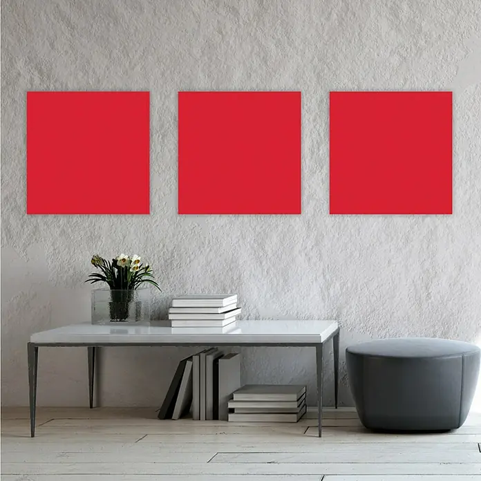 Jangal Wandpaneel Modular Wall PET Filz - Red, 520 x 520 x 6 mm - Eine Nahaufnahme von drei roten quadratischen Kunstwerken, die an einer strukturierten Wand über einem minimalistischen Tisch mit Büchern und einem Hocker hängen.