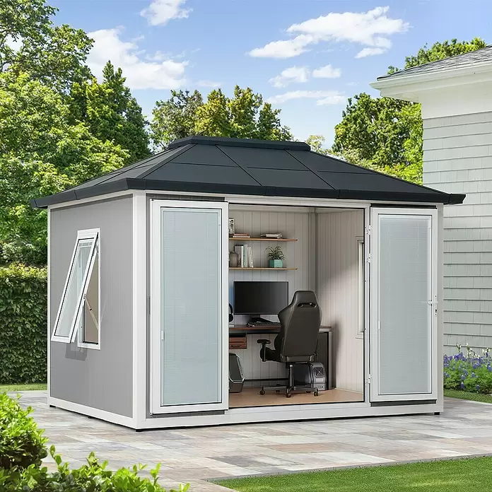 Sunjoy Gartenhaus Riga - Außenmaß inkl. Dachüberstand (B x T): 302 x 296 cm, Stahl, Dunkelgrau - Graues Gartenbüro mit schwarzem Dach und weißem Rand, offen auf einer Terrasse. Innen schaffen Schreibtisch, Computer und Stuhl einen externen Arbeitsplatz.