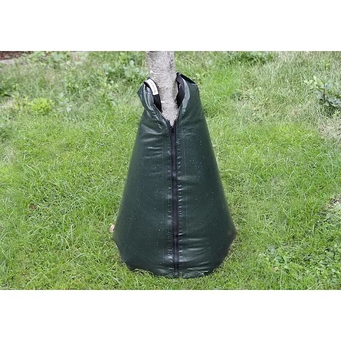 Floraworld Bewässerungssack Classic - Passend für: Bäume bis Ø 18 cm, 190 g/m² - Ein grüner Bewässerungssack um einen Baumstamm auf einer Rasenfläche, der zur langsamen Bewässerung junger Bäume dient.