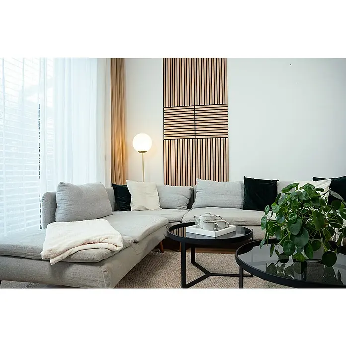 Jangal Akustikpaneel Modular Wall Furnier - Fanal Oak, 1.040 x 520 x 10 mm - Helle und moderne Inneneinrichtung mit großem Ecksofa, Holzwandpaneel und zwei runden Couchtischen, die ein gemütliches Ambiente schaffen.