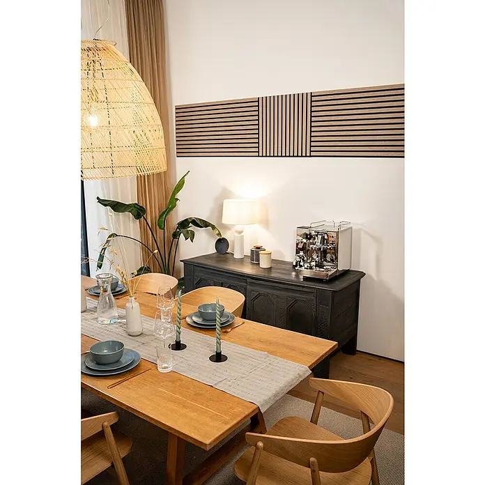 Jangal Akustikpaneel Modular Wall Furnier - Davert Oak, 520 x 520 x 10 mm - Das Bild zeigt ein stilvolles Esszimmer mit einem Holztisch und passenden Stühlen, dekoriert mit Geschirr und Kerzen. An der Wand hängt ein modernes Holzpaneel.