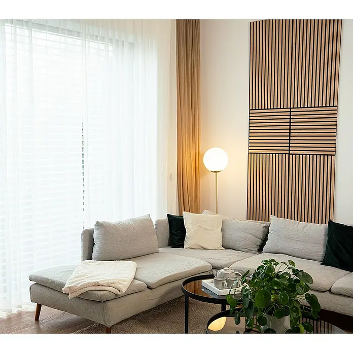 Jangal Akustikpaneel Modular Wall Furnier - Fanal Oak, 1.040 x 520 x 10 mm - Ein Wohnzimmer mit einem grauen Ecksofa, einer Stehlampe und einer dekorativen Holzpaneele an der Wand.