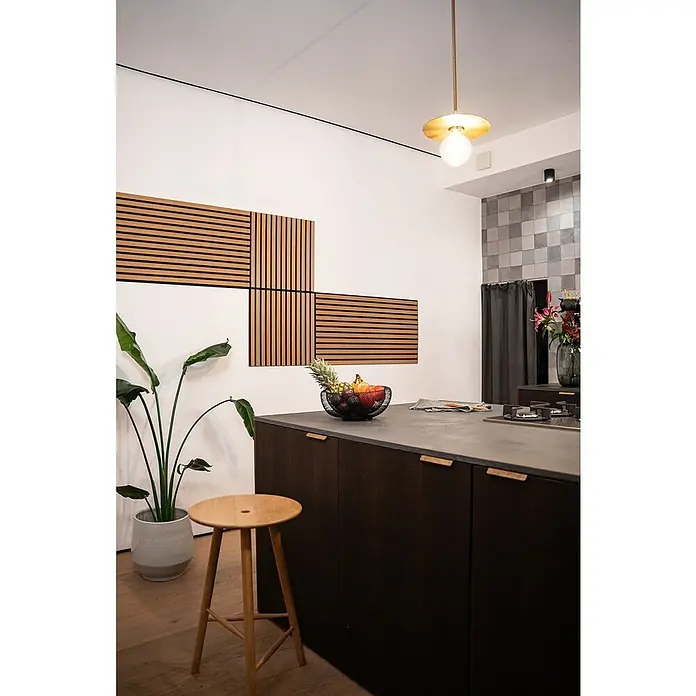 Jangal Akustikpaneel Modular Wall Furnier - Davert Oak, 520 x 520 x 10 mm - Küchenstillleben mit einem dunklen Küchenblock, einem Holzhocker und einer dekorativen Wandgestaltung, beleuchtet von einer modernen Hängelampe.