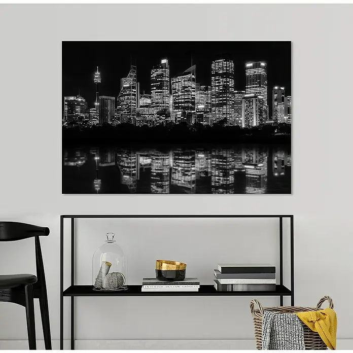 Glasbild - New York, B x H: 90 x 60 cm - Wandbild mit Schwarzweiß-Skyline-Motiv, das über einem schwarzen Regal mit Deko-Objekten und Büchern hängt, für ein modernes Wohnambiente.