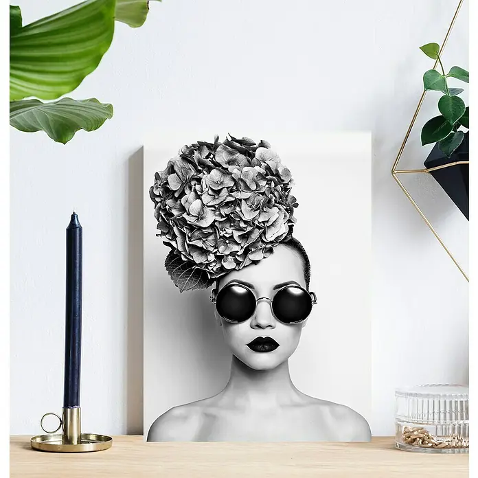 Glasbild - Frau mit Blumenhut, B x H: 80 x 120 cm - Schwarz-Weiß-Porträt einer Frau mit Sonnenbrille und Blumenhut, das auf einer hellen Holzoberfläche steht und eine moderne, stilvolle Dekoration darstellt.