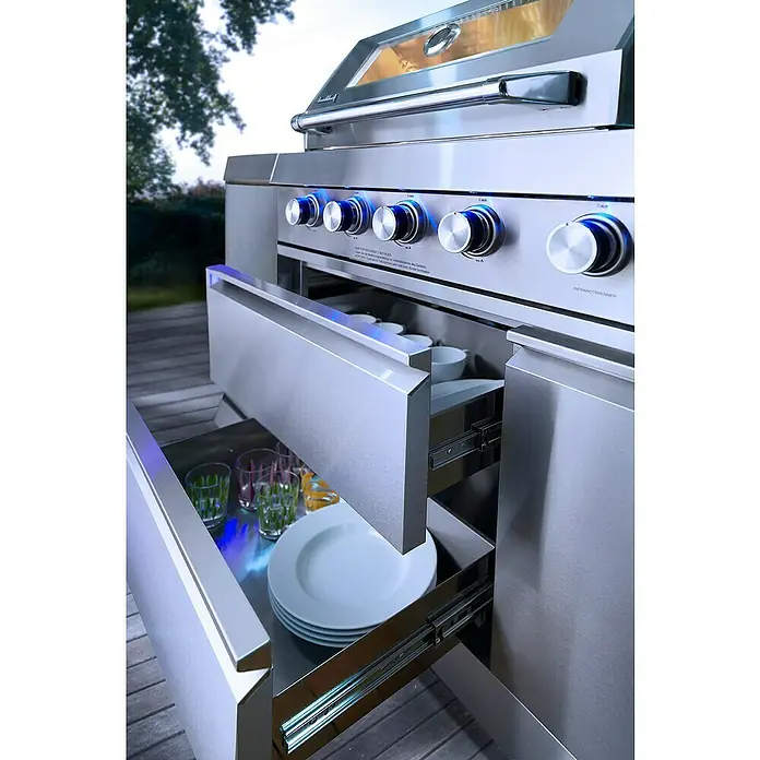 Buschbeck Outdoorküche Oxford - Edelstahl, Anzahl Brenner: 4 - Edelstahlgrill mit geöffneten Schubladen, die Geschirr und Gläser zeigen. Die blauen Lichter heben das moderne Design hervor.