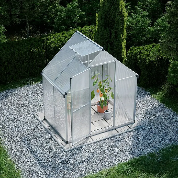Geo garden Gewächshaus Paris - Außenmaß inkl. Dachüberstand (B x T): 178,2 x 113,2 cm, Silber - Das Bild zeigt ein Gewächshaus im Garten mit einer Pflanze und einer Gießkanne darin. Kies und Grün umgeben es.